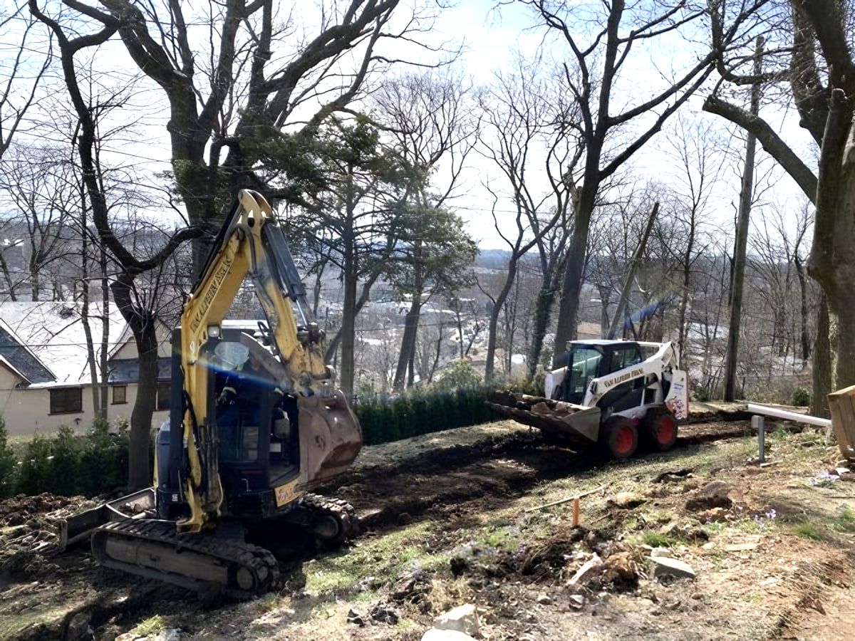 Excavator and skid steer clearing wooded hillside lot